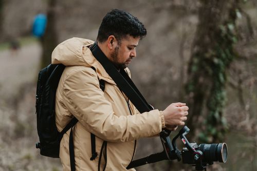 Free A professional photographer in a beige jacket adjusting his camera in a natural outdoor setting. Stock Photo