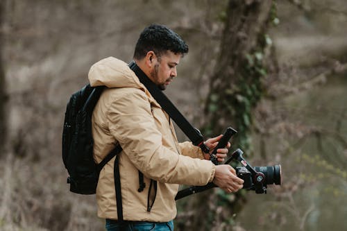 A man with a camera and backpack standing near a river