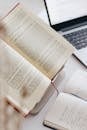 An Open Book and a Notebook Lying next to a Laptop