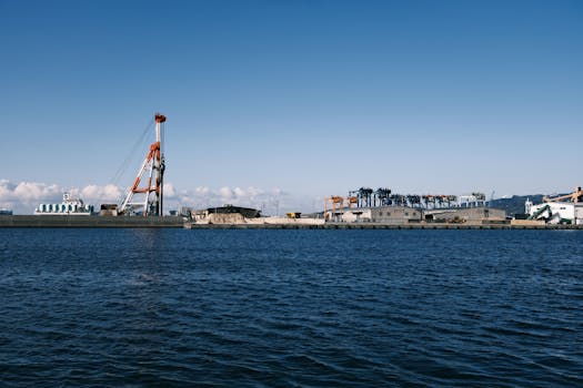View of an industrial port in Gamagōri, Japan, showcasing cranes and the coastal area under a clear sky.