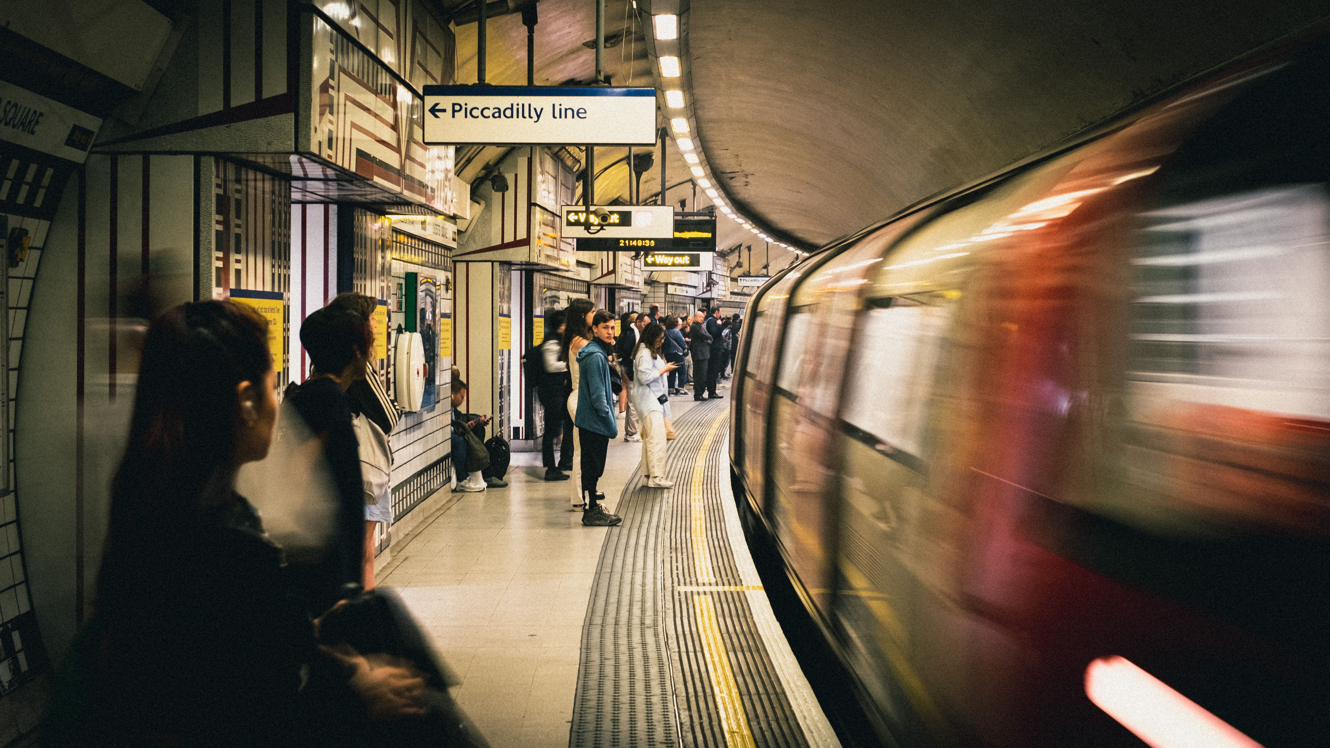 Commuters waiting at a vibrant London Underground station on the Piccadilly Line.
