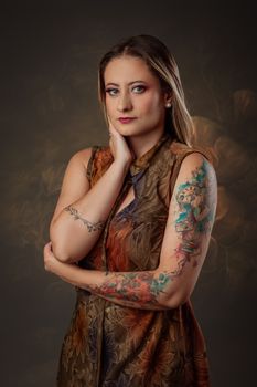 Portrait of a young woman with tattoos in a stylish dress posing elegantly in a studio.