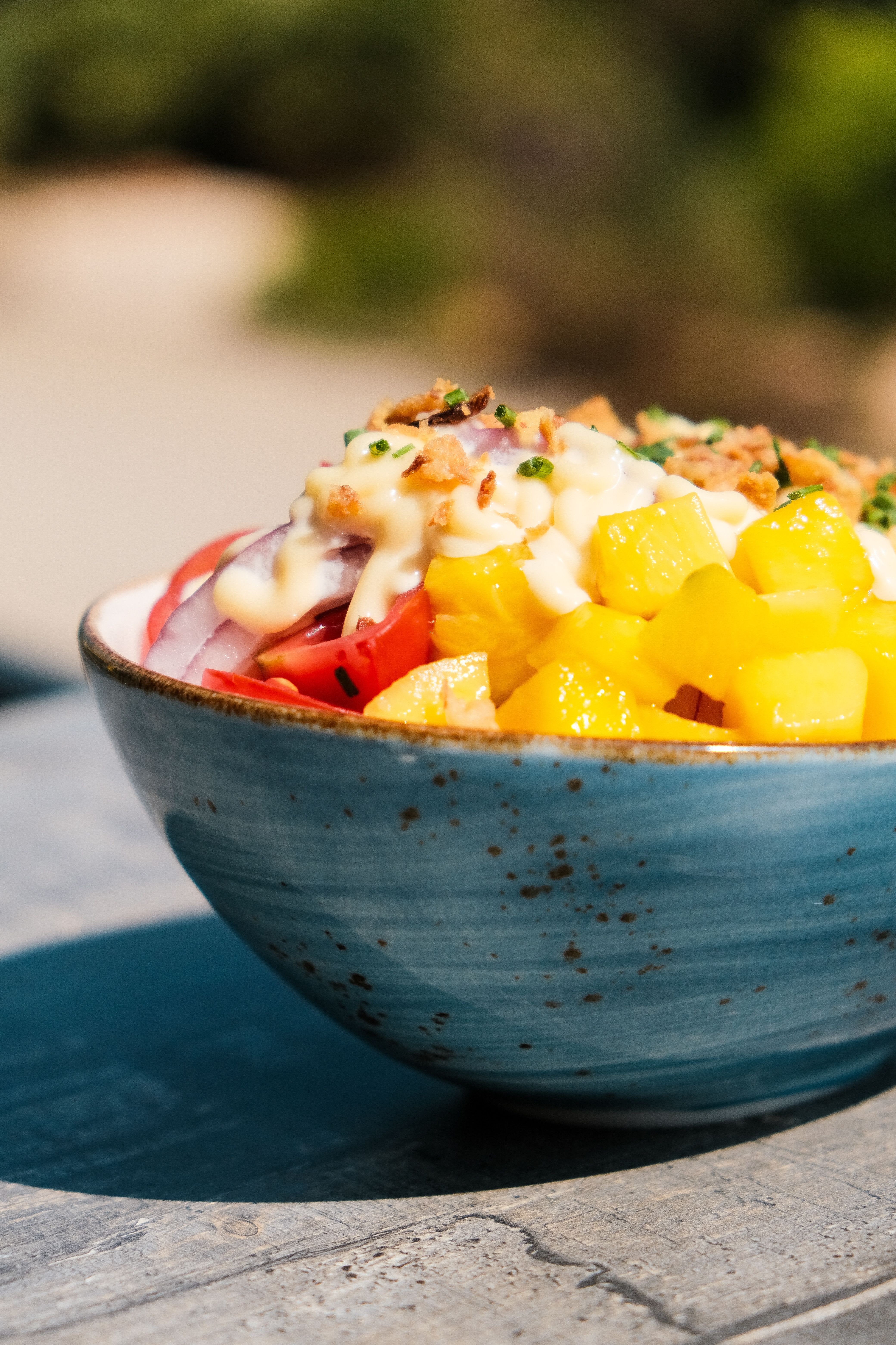A brightly colored vegetable salad with dressing served in a blue ceramic bowl outdoors