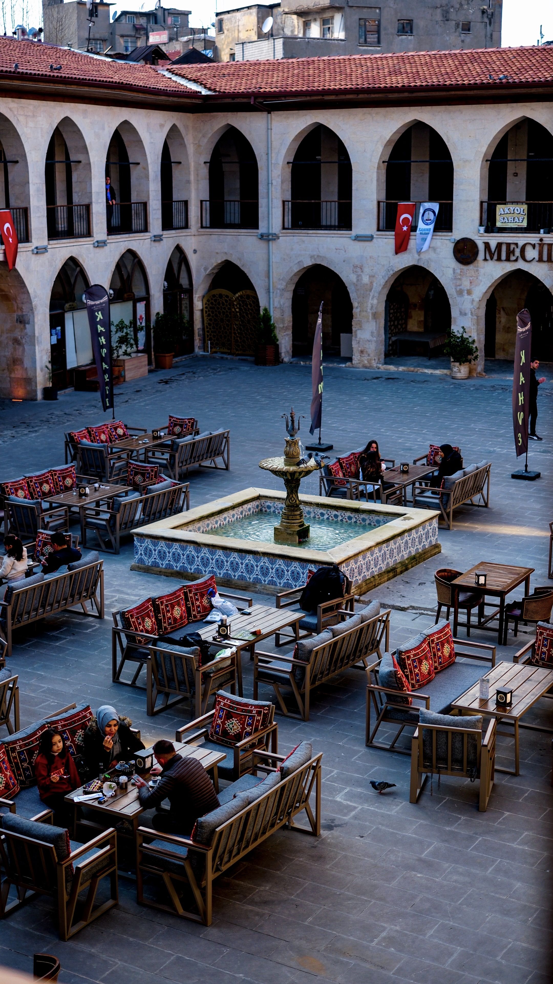 Charming courtyard in Mecidiye Han, Gaziantep, Türkiye with classic architecture and dining setup.
