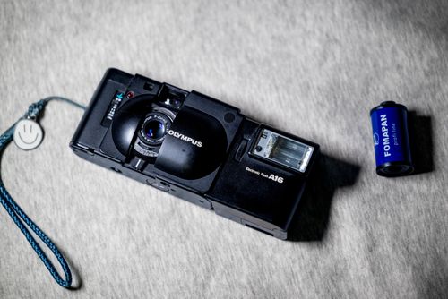 Free A vintage Olympus camera with a Fomapan film roll on a textured gray surface. Stock Photo