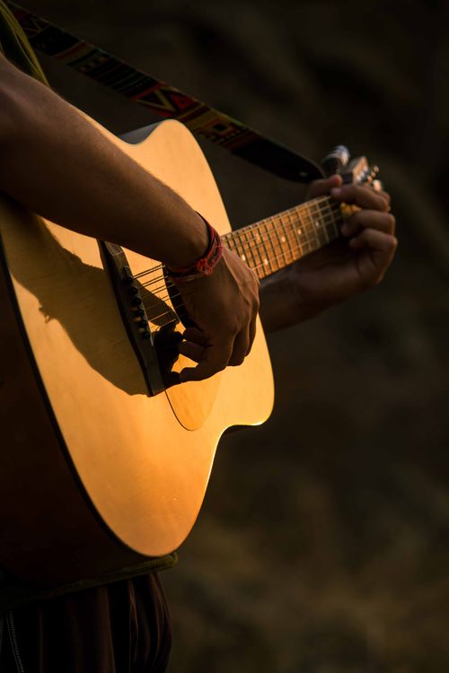 Free Detailed image of hands strumming an acoustic guitar outdoors in a warm, natural setting. Stock Photo