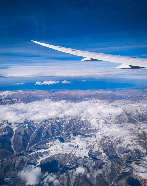 Free Stunning view of snow-covered mountains seen from airplane window, showcasing vast landscape and clear blue sky. Stock Photo