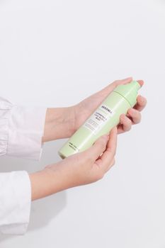 Close-up of woman's hands holding a besoma bottle on white background.
