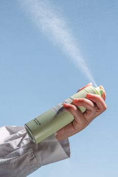 Person's hand spraying deodorant in front of a clear sky, product shot.