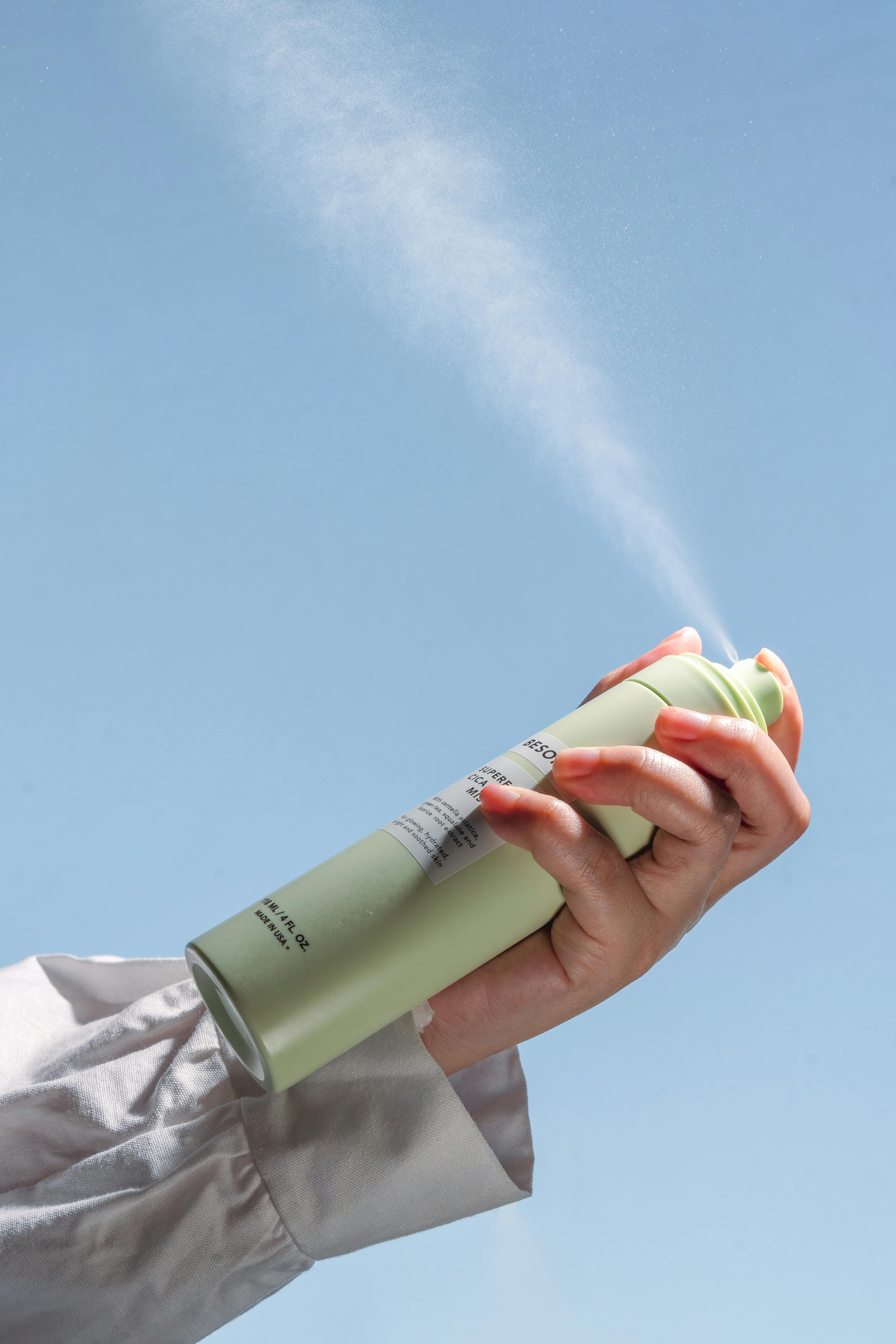 Free Person's hand spraying deodorant in front of a clear sky, product shot. Stock Photo