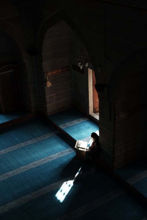 Free A person sits peacefully, reading in a quiet, dimly lit mosque interior. Stock Photo