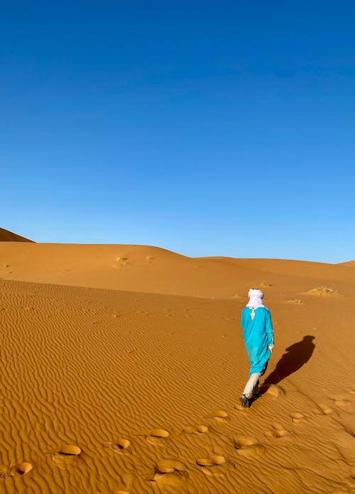 A person walking in the desert with a blue scarf