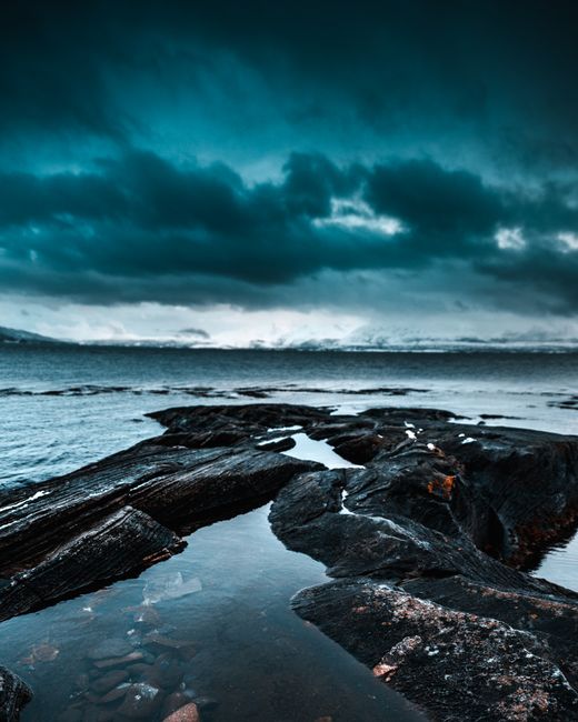 Moody seascape in Tromsø, showcasing rugged rocks and cloudy skies over the ocean.