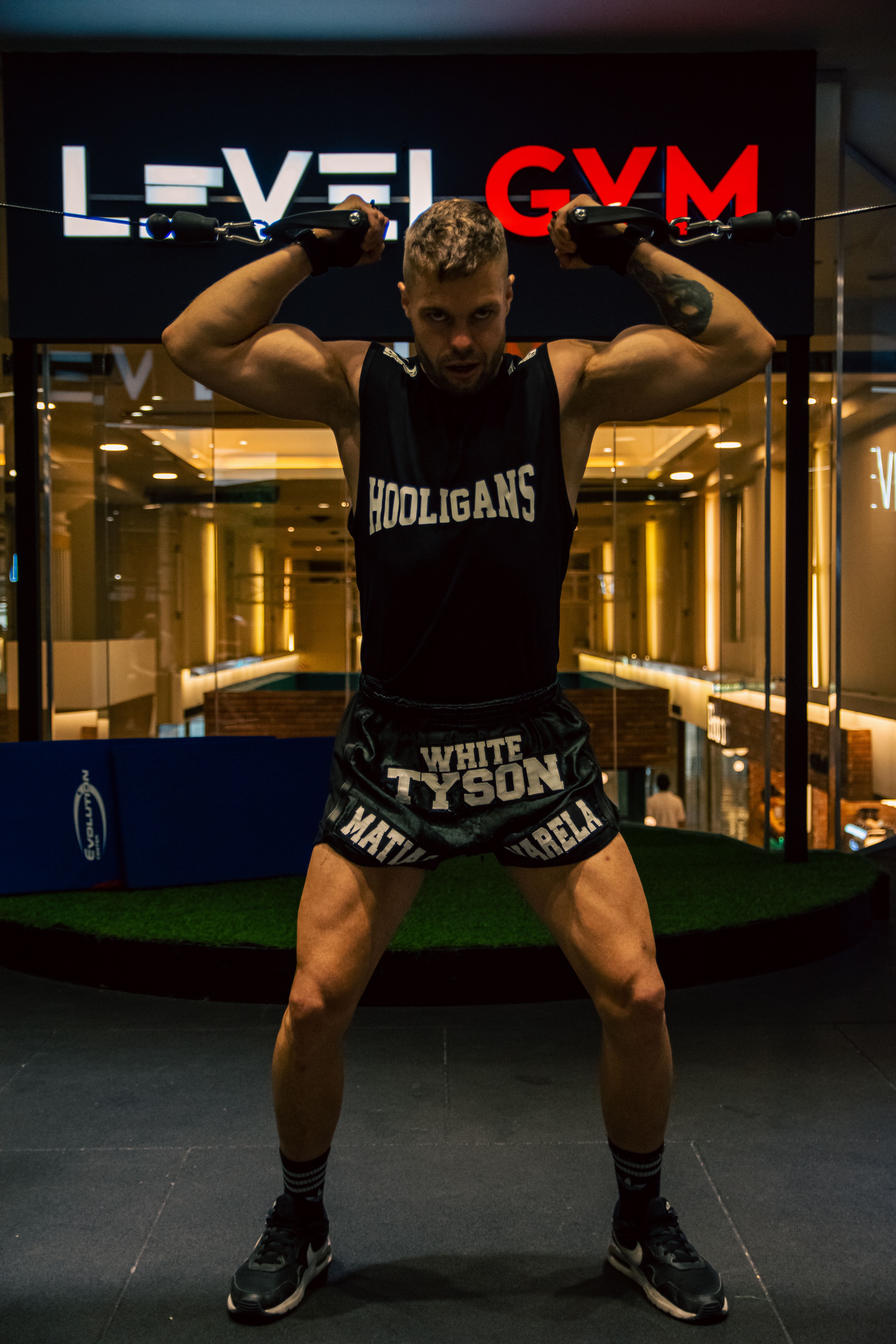 A muscular man stands in a gym lifting equipment, showcasing fitness and strength.