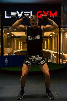 A muscular man stands in a gym lifting equipment, showcasing fitness and strength.
