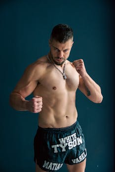 Strong and muscular man posing as a boxer with fists raised in a studio.