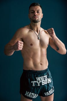 Shirtless male boxer posing in fighting stance against blue background.