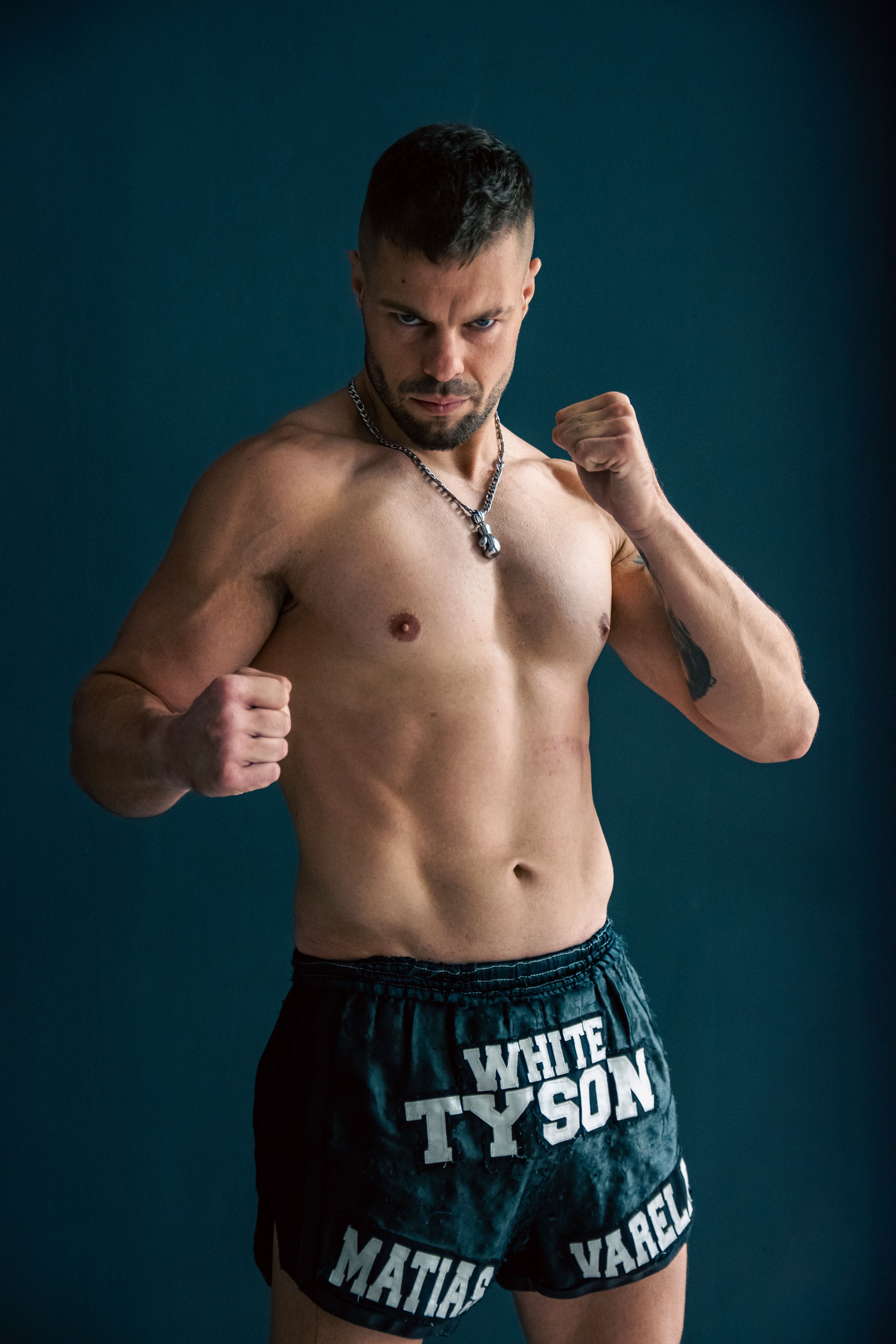 A muscular man poses shirtless, showcasing a strong stance and athletic build against a dark background.