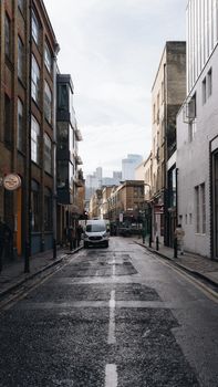 A city street view combining classic and modern architecture with a van on a wet road.