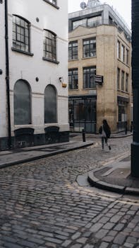 A person walking on a cobblestone street between urban buildings.