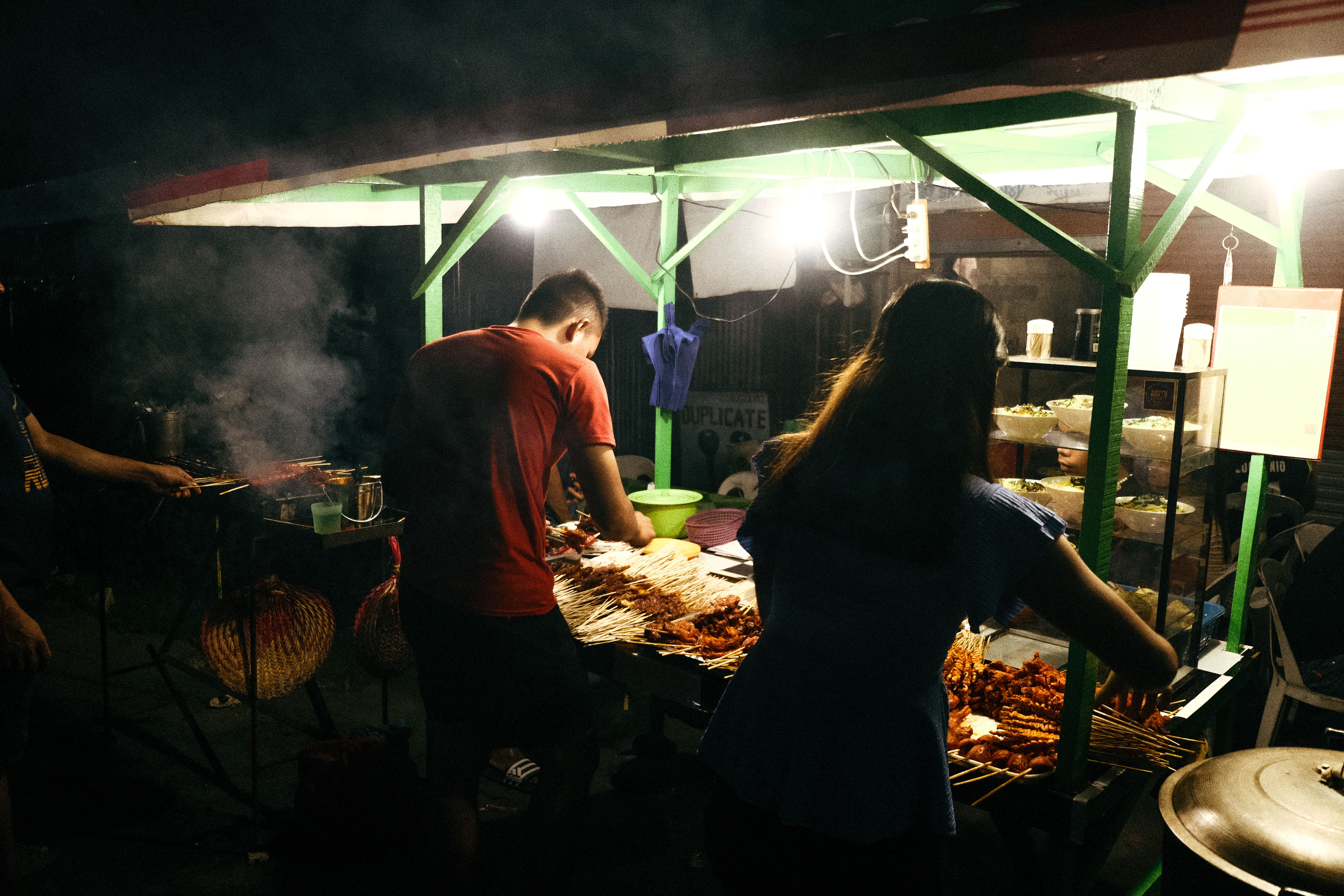 Night scene of street food vendors grilling skewers under lights, creating a cozy ambiance.