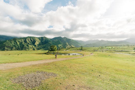 Expansive rural landscape with green hills and a serene lake under a cloudy sky.