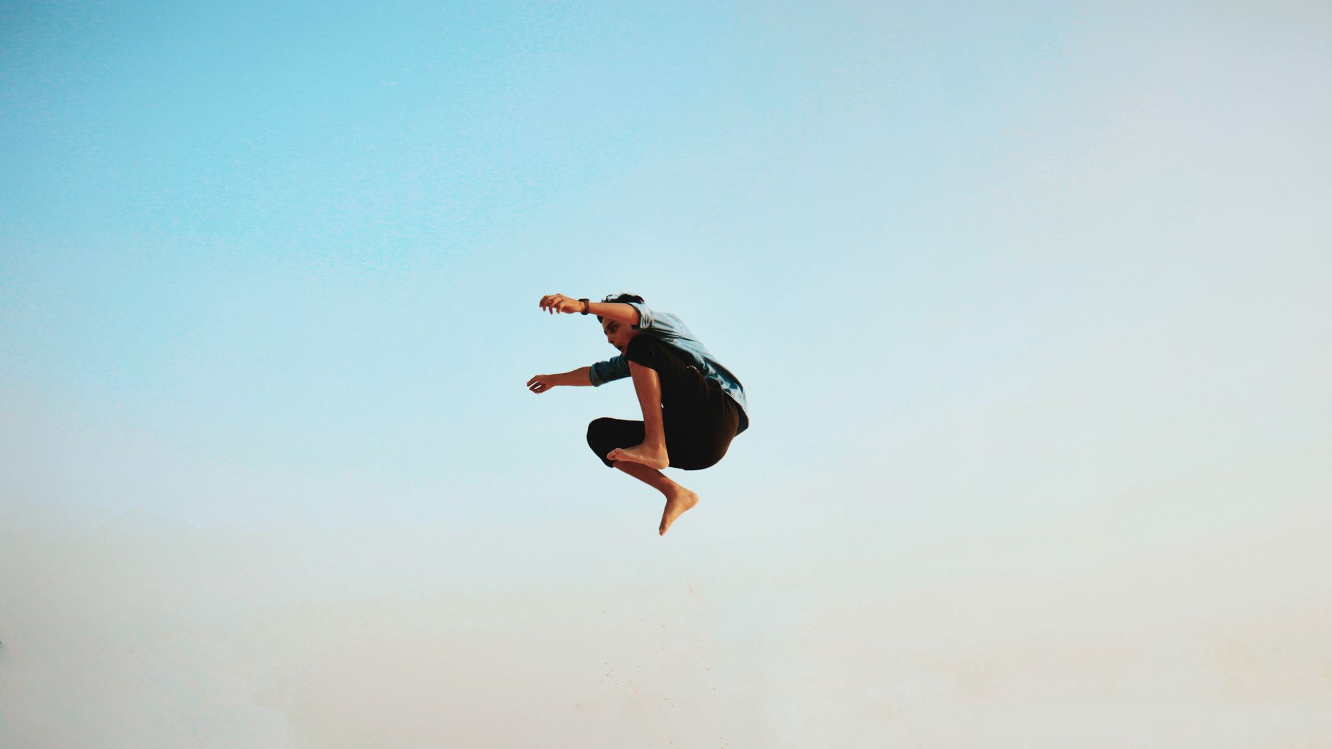 A man energetically jumps midair with a clear blue sky backdrop, capturing a sense of freedom.