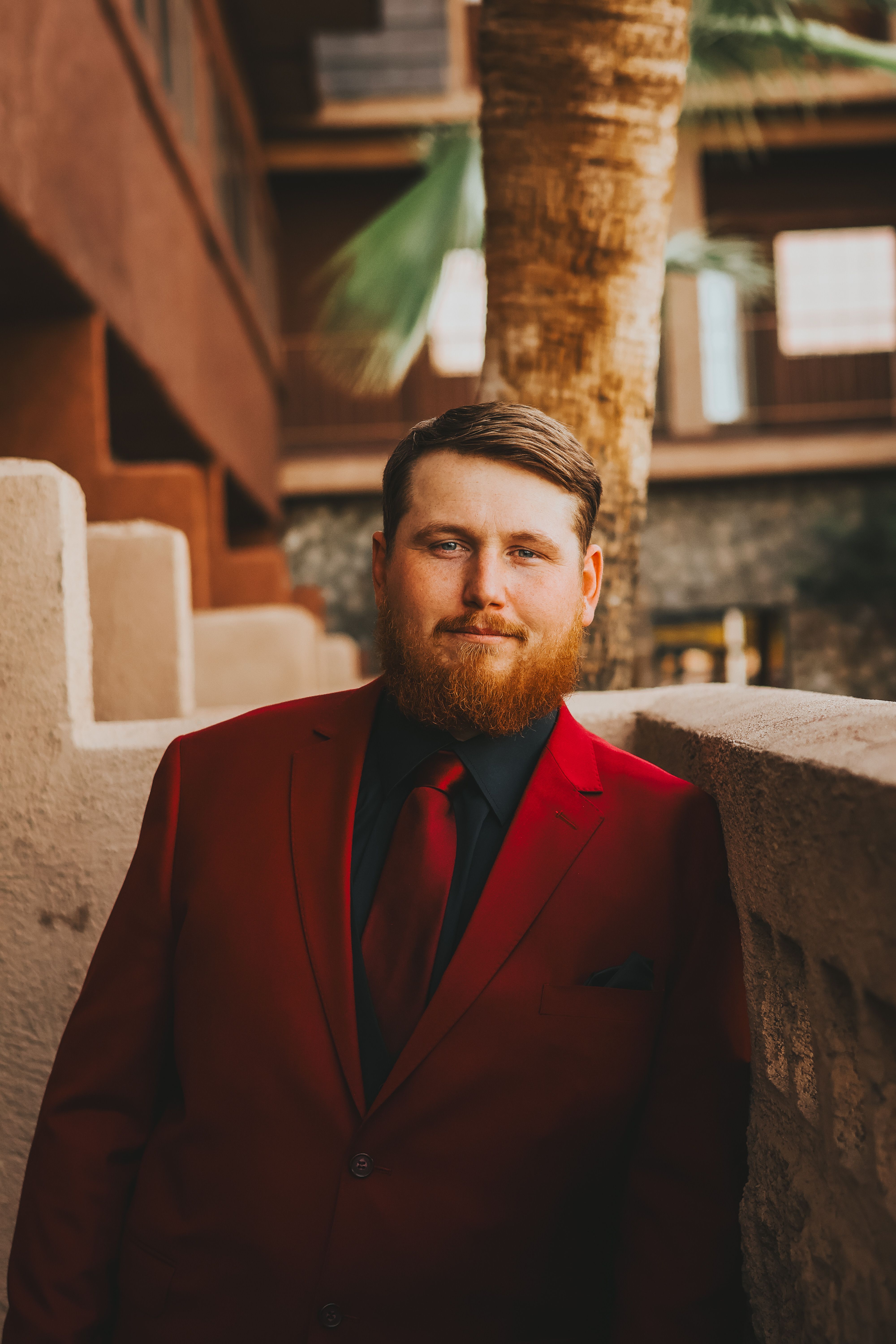 Portrait of a man in a red suit with a beard standing against an urban backdrop.
