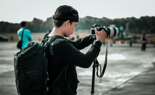 Free A male photographer setting up his tripod and camera outdoors on an airfield, focused on capturing a perfect shot. Stock Photo