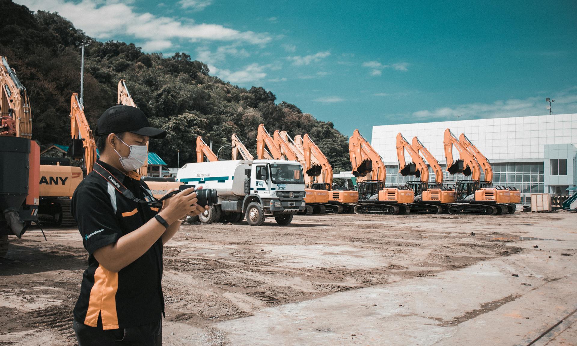 A photographer takes photos at a construction site with heavy machinery and trucks on a sunny day.