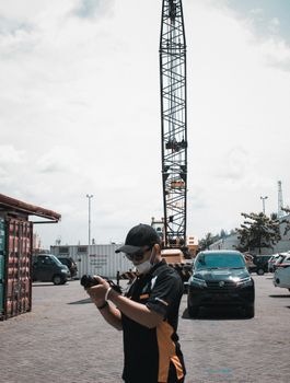 Man taking photos in a cargo port with cranes and vehicles around.