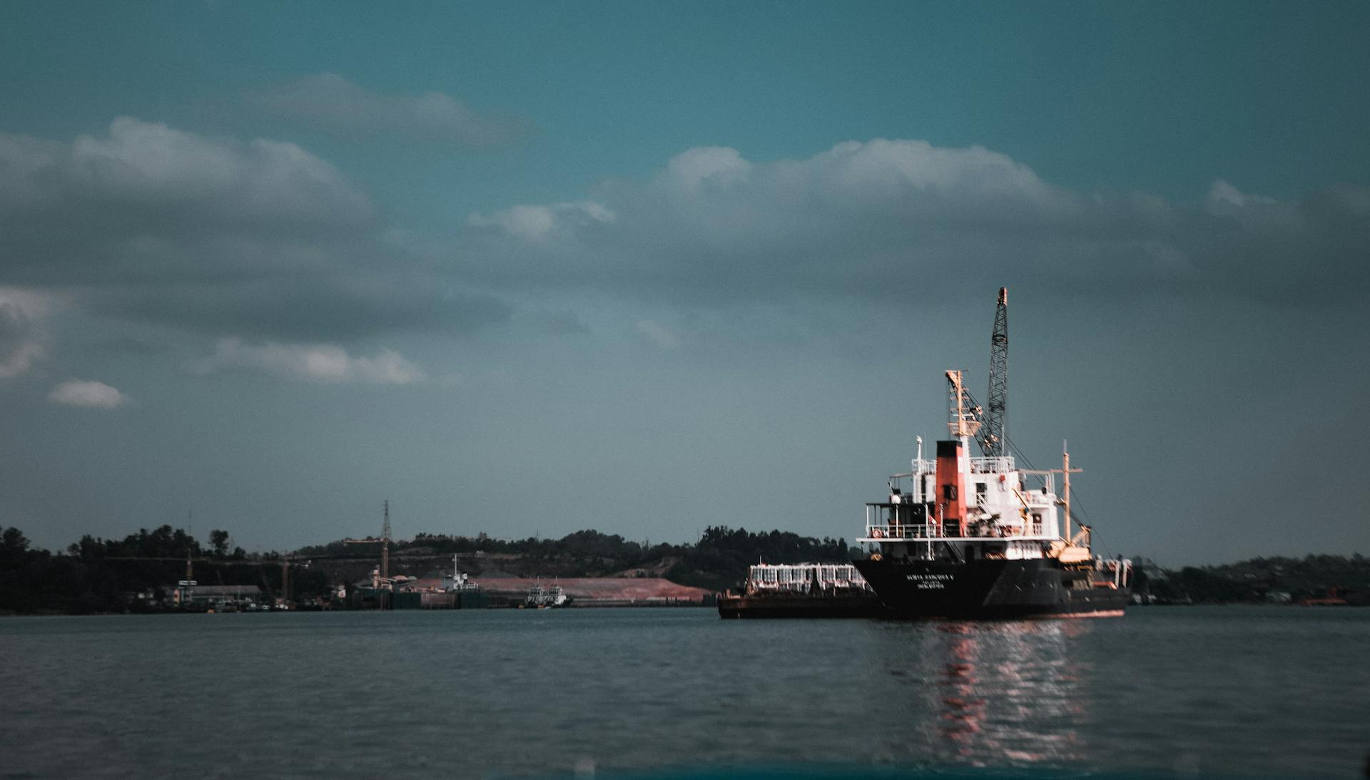 A cargo ship docked at an industrial port under a cloudy sky.