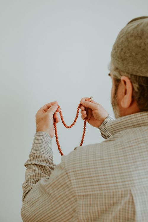 Free An elderly man wearing a hat holds prayer beads, symbolizing faith and devotion. Stock Photo