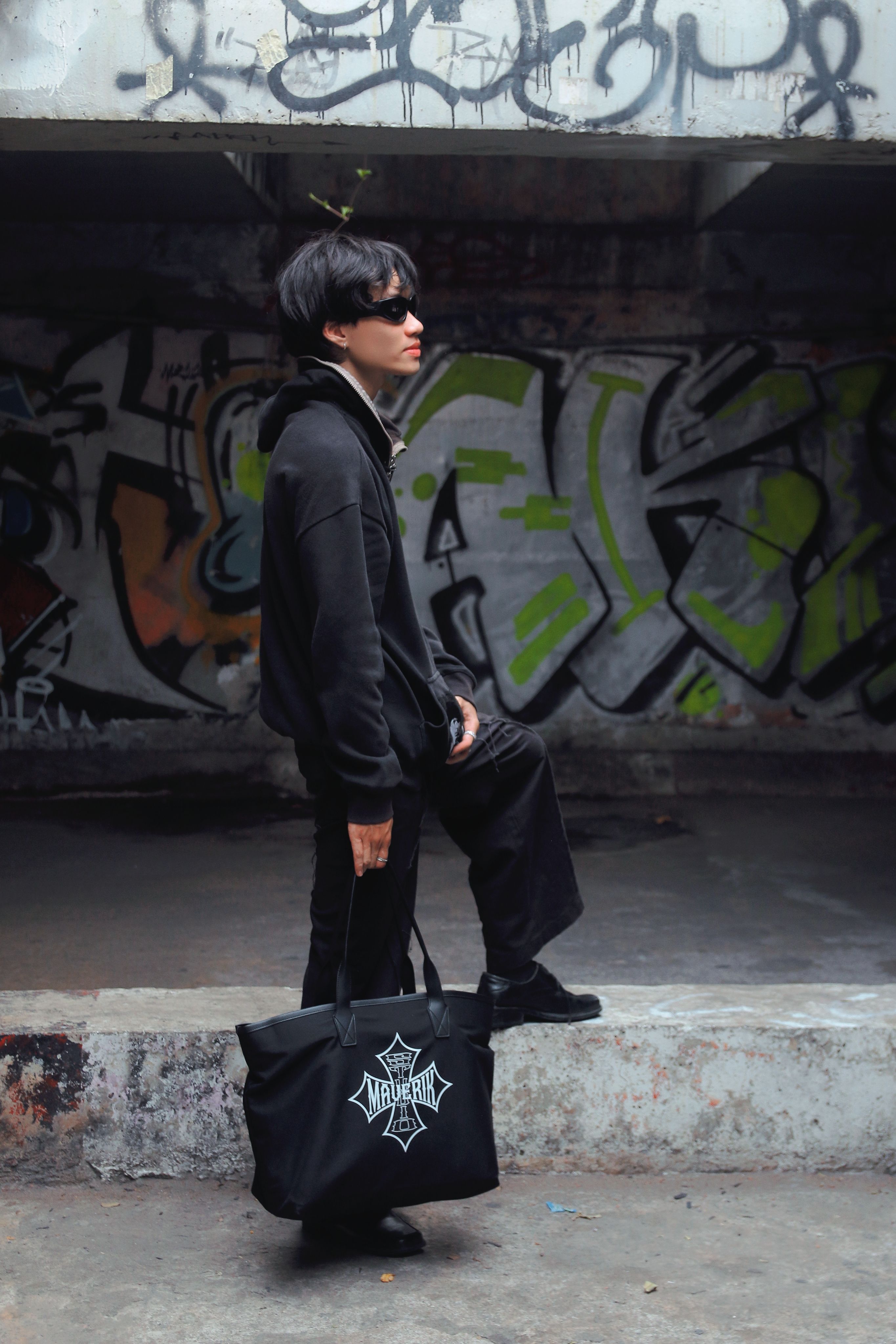Stylish man in black attire poses against vibrant graffiti wall, embodying urban fashion trends.