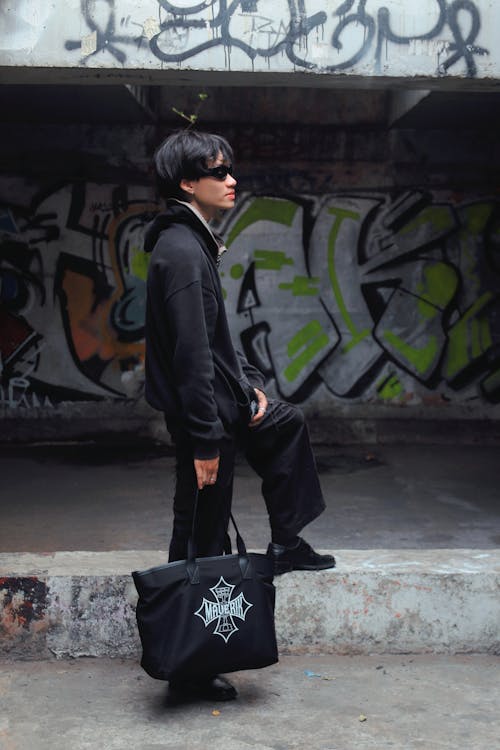 A man in black jacket and sunglasses holding a tote bag