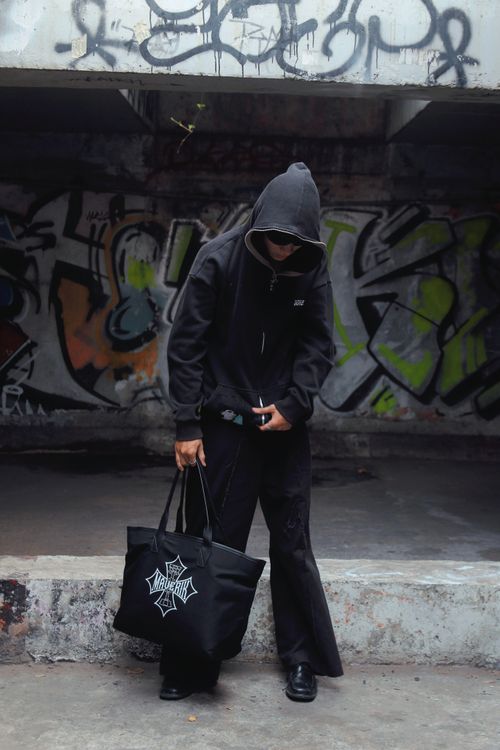 Free Model wearing a black hoodie in an urban setting with colorful graffiti, holding a tote bag. Stock Photo