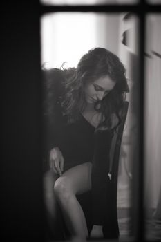 A graceful woman sits elegantly by a window in a black and white setting.