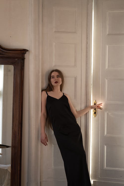A woman in a black dress leaning against a door