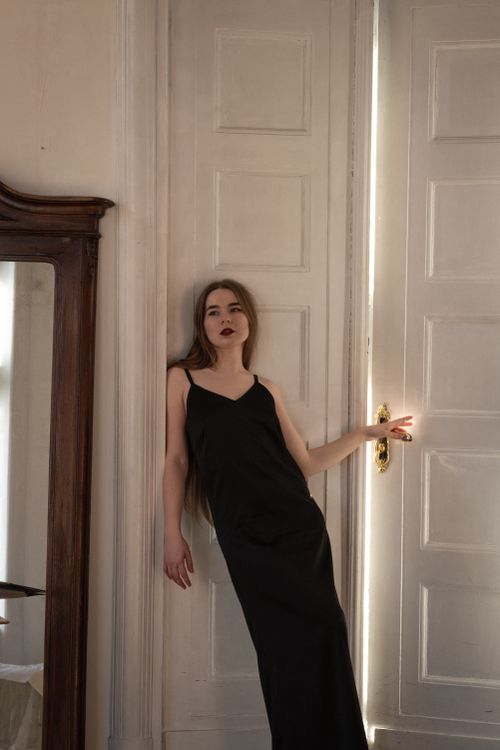 Free A woman in a black dress poses elegantly against a closed door with soft lighting. Stock Photo