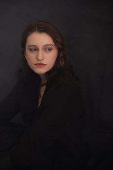 A young woman posing elegantly in a black suit, looking away in a studio setting.