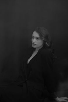 Black and white portrait of a young woman in a black suit, sitting in a serene pose.