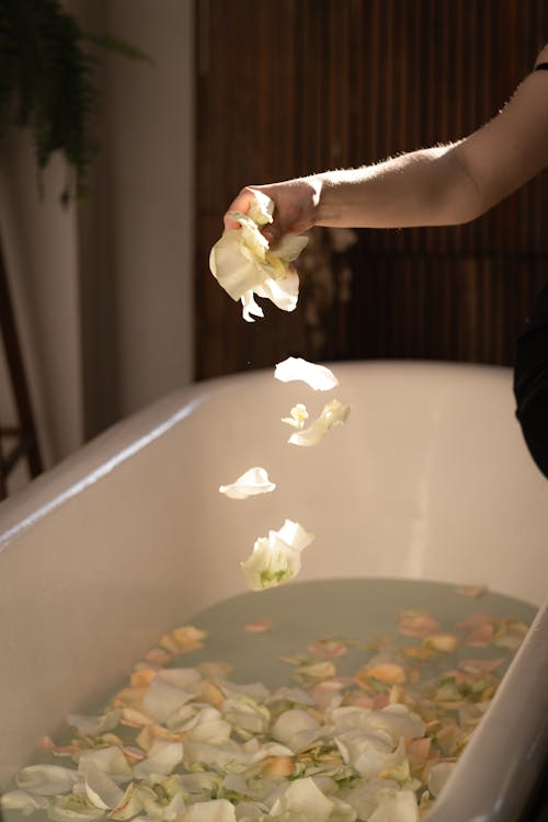 A woman is pouring rose petals into a bathtub