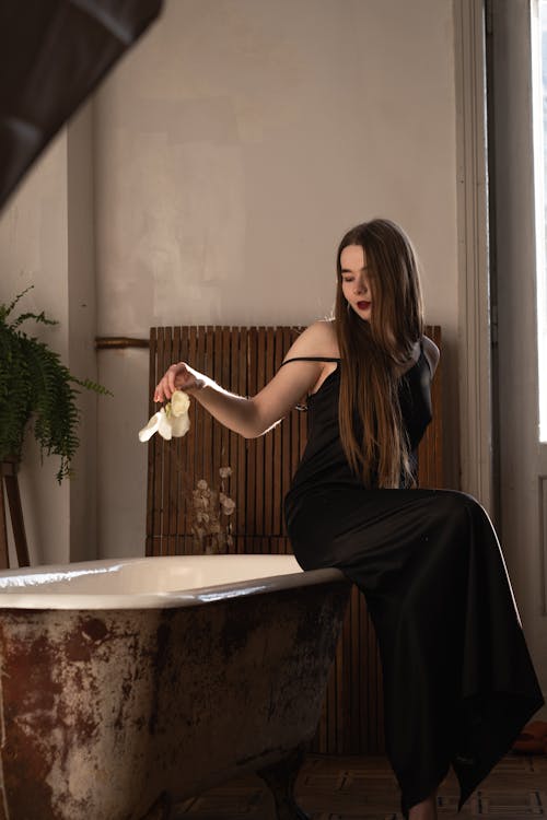 A woman in a black dress is sitting on a bathtub