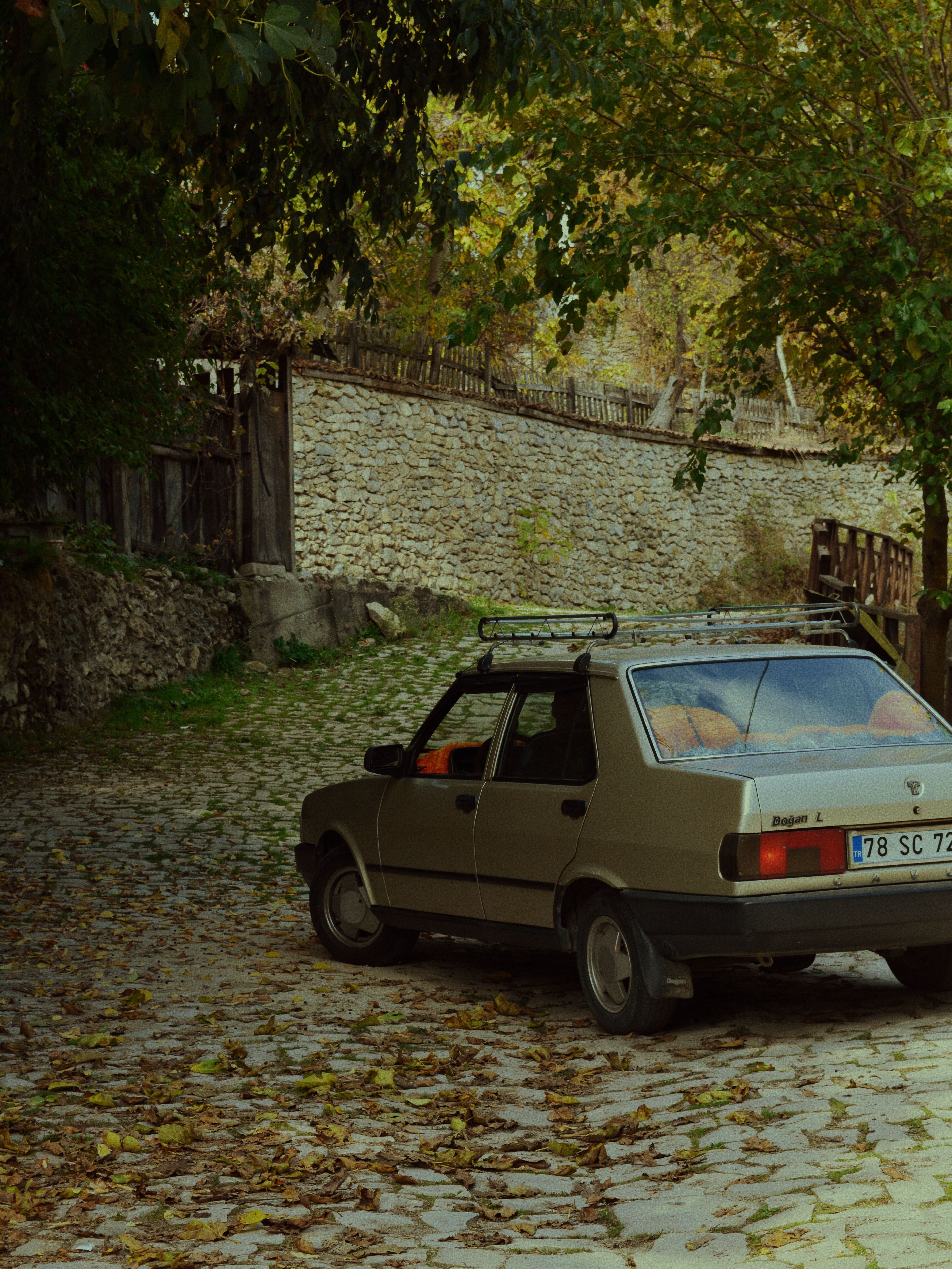 A vintage car parked on a cobblestone street surrounded by autumn leaves and stone walls.