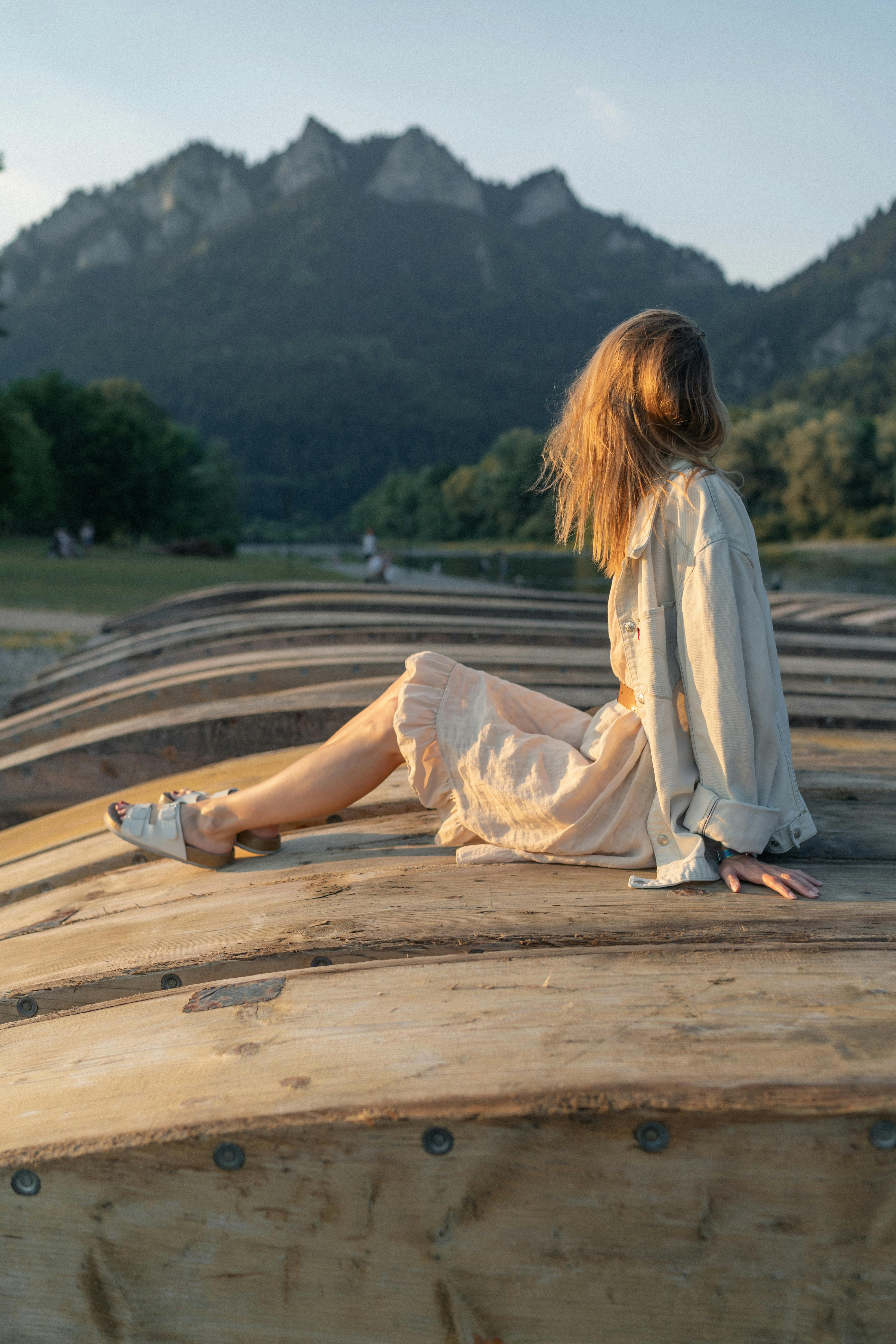 Woman in a sundress sits on a wooden surface, enjoying a peaceful mountain view in Sromowce Niżne, Poland.