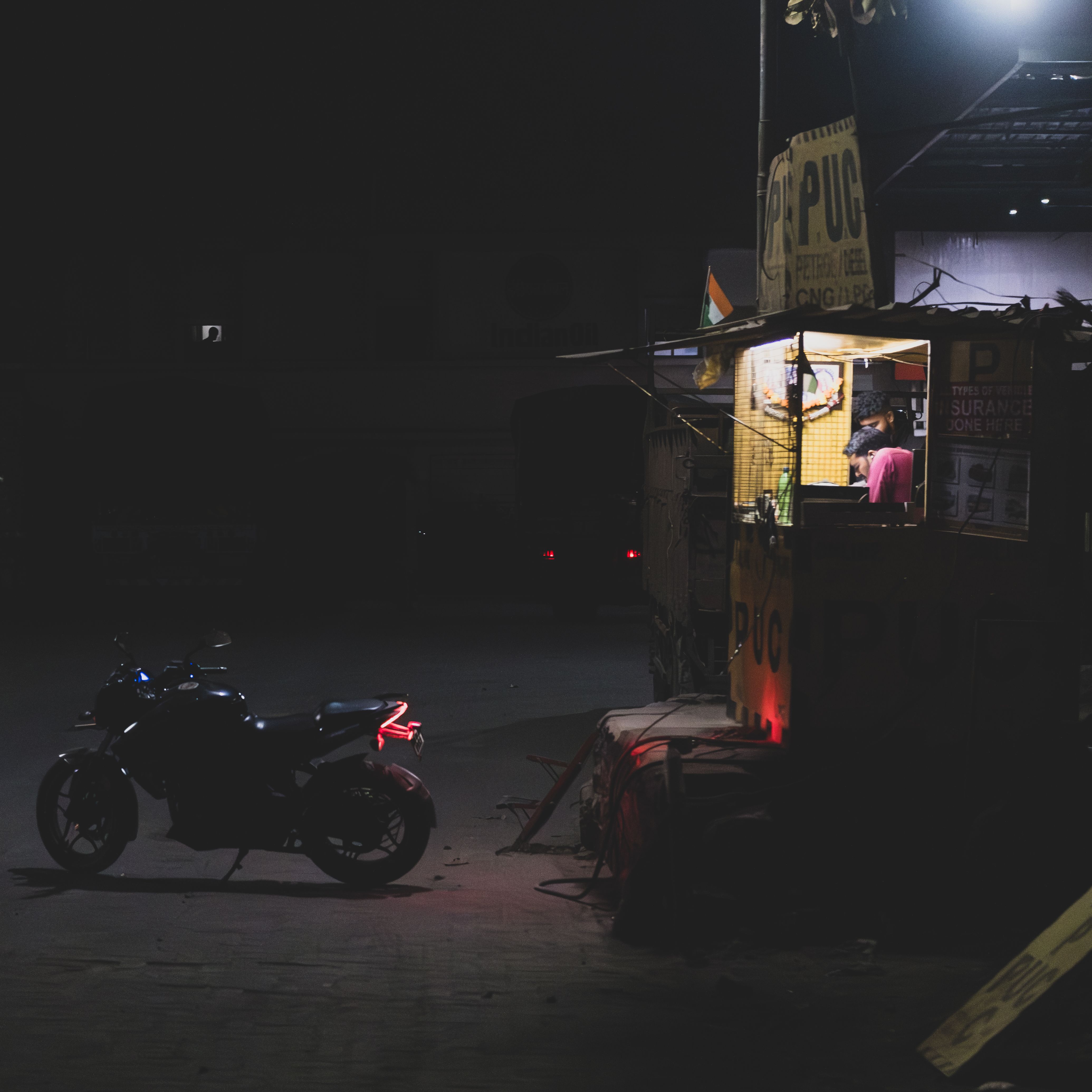 A dimly lit urban street scene featuring a food stand and parked motorcycle at night.