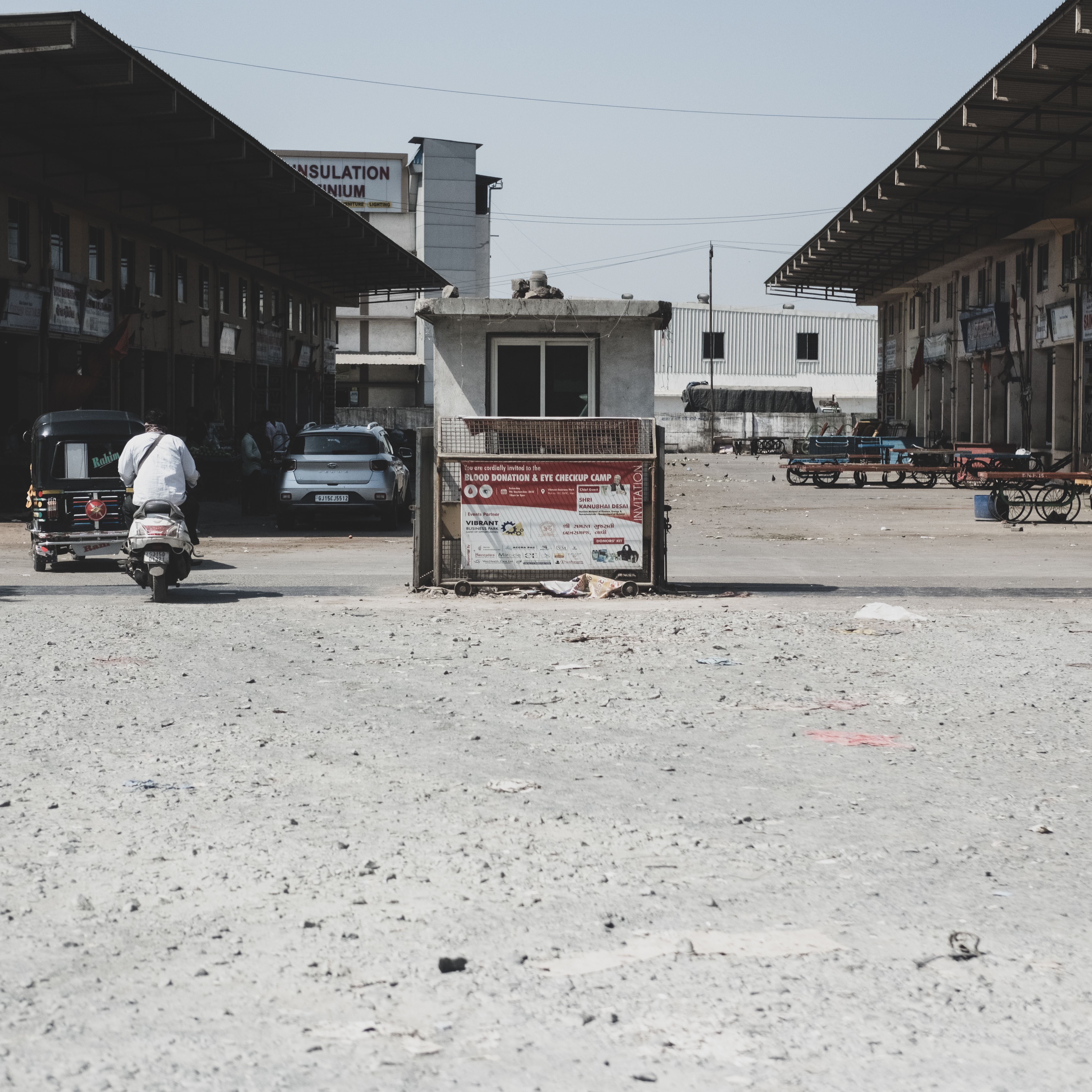 A scene of an industrial area with a motor scooter rider passing by warehouses on a sunny day.