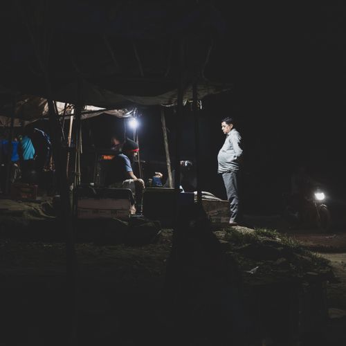 Free A rural village night market with people gathered around under dim lights, creating a moody atmosphere. Stock Photo