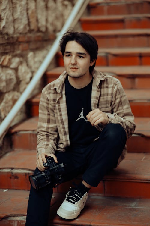 A young man sitting on some steps with a camera