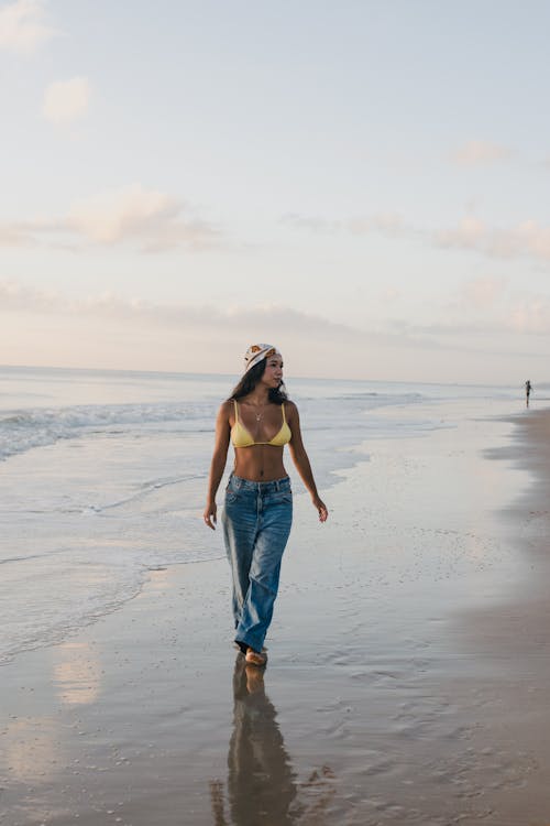 A woman walking on the beach in a yellow top and jeans